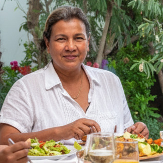 Icon image of a woman seated at the dinner table engaged in conversation with others off-camera.